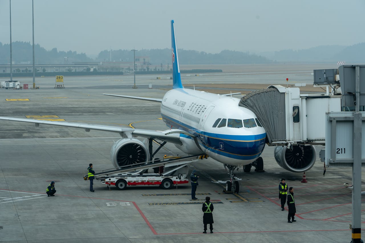 Passenger airplane docked at airport terminal with crew members working around it.